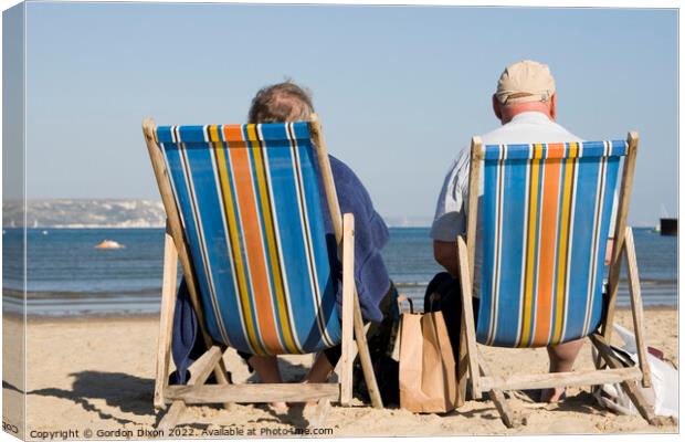Elderly couple in bright striped deckchairs on the sand at Weymouth Canvas Print by Gordon Dixon