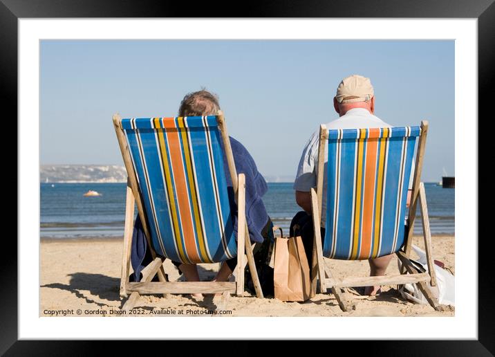 Elderly couple in bright striped deckchairs on the sand at Weymouth Framed Mounted Print by Gordon Dixon