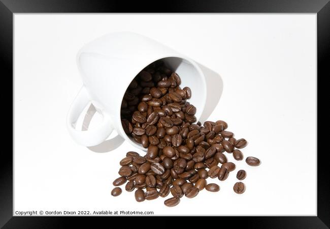 Roasted coffee beans spilling out of a mug - white background Framed Print by Gordon Dixon