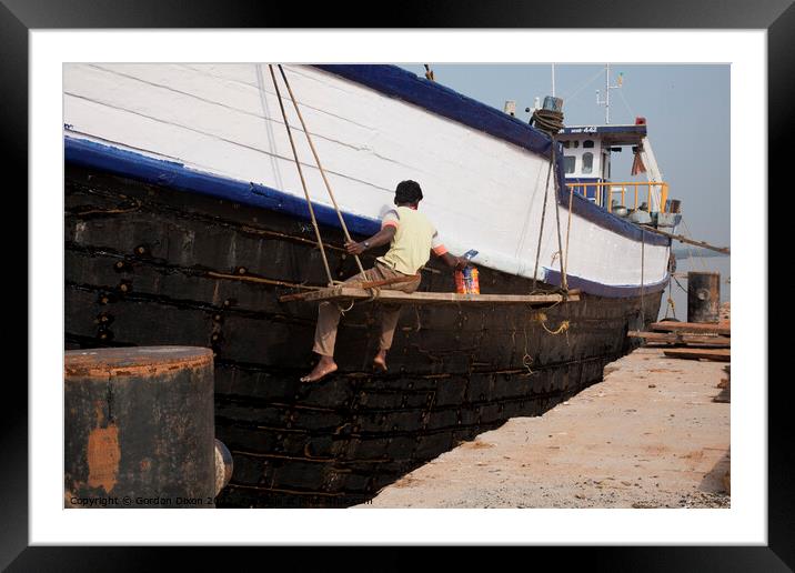 A ship repairer paints an old wooden ship in Mangalore, India Framed Mounted Print by Gordon Dixon