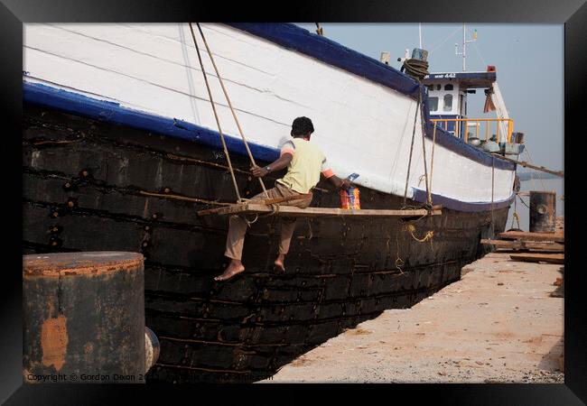 A ship repairer paints an old wooden ship in Mangalore, India Framed Print by Gordon Dixon
