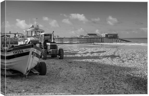 Black and white vintage photo of fishing boats and equipment on Cromer beach on the North Norfolk Coast. In the distance is the Victorian era pier Canvas Print by Chris Yaxley