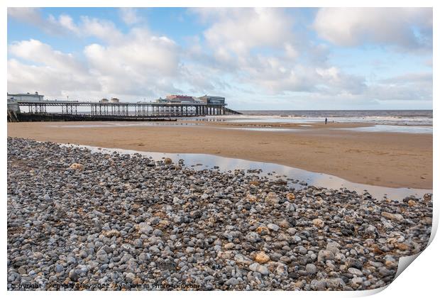 View across a sand and shingle beach with a distant pier in the background Print by Chris Yaxley