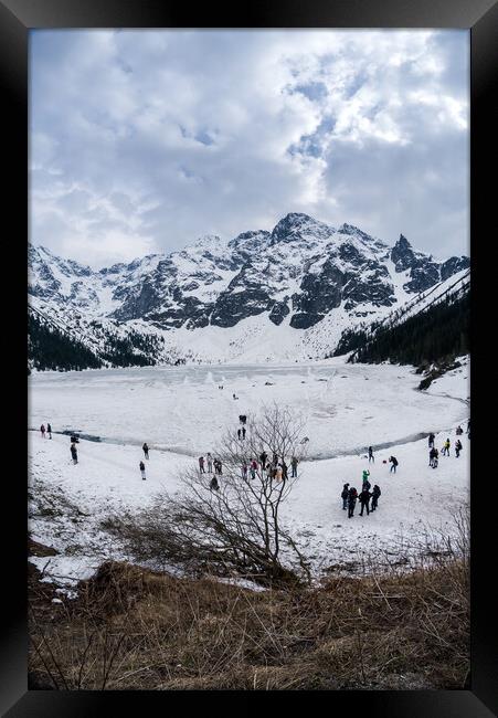 Zakopane, Poland - May 04, 2022: Panorama of Morskie oko frozen lake covered with snowy tatra mountains with people or tourists walking on snow Framed Print by Arpan Bhatia