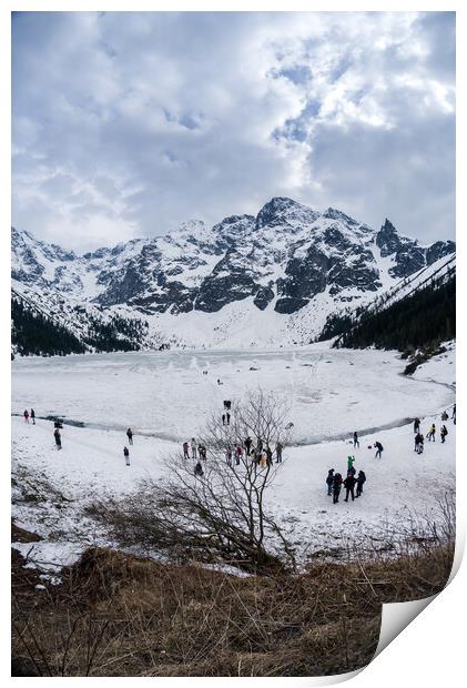 Zakopane, Poland - May 04, 2022: Panorama of Morskie oko frozen lake covered with snowy tatra mountains with people or tourists walking on snow Print by Arpan Bhatia