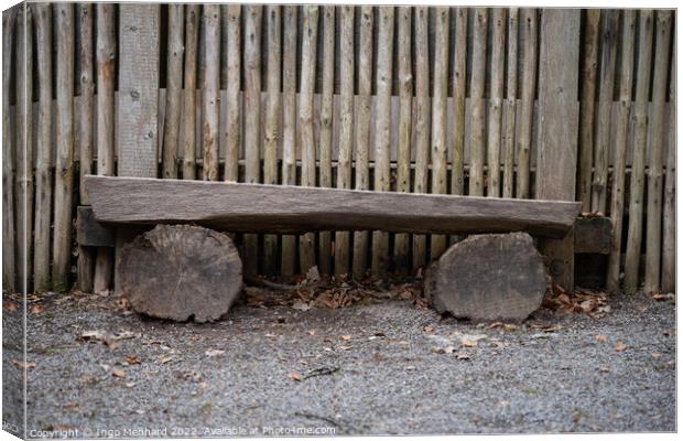 Bench made with logs of wood by a wooden fence Canvas Print by Ingo Menhard