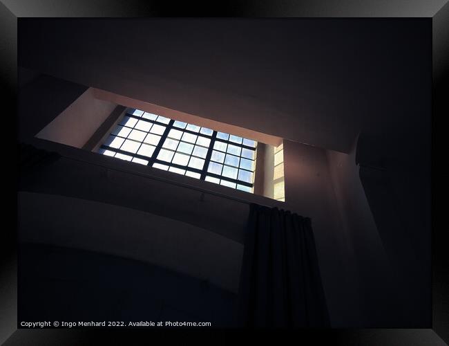 A low-angle shot of a small square window with bars in the dark room Framed Print by Ingo Menhard
