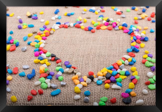 Colorful pebbles form a heart shape on canvas grou Framed Print by Turgay Koca