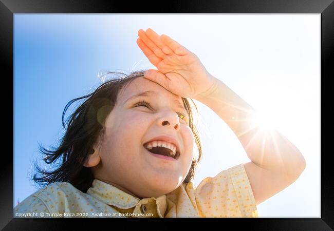 Happy smiling boy in flare sunshine with  hand at forehead Framed Print by Turgay Koca