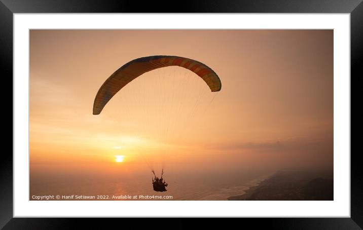 Tandem paragliding over sea and beach while golden Framed Mounted Print by Hanif Setiawan
