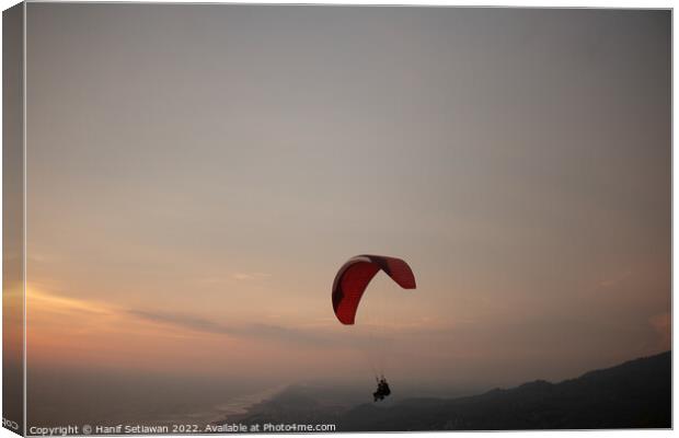 Tandem paragliding over sea and beach at sunset Canvas Print by Hanif Setiawan