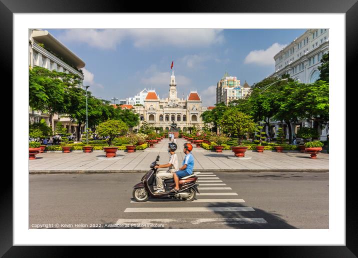 A motorcyclist rides along the road.past a statue of Ho Chi Minh Framed Mounted Print by Kevin Hellon