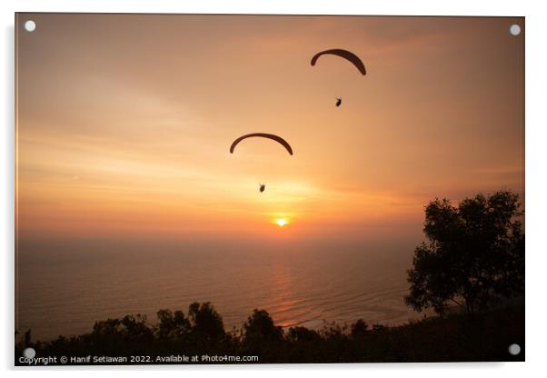 Two paraglider over treetops and ocean at sunset Acrylic by Hanif Setiawan