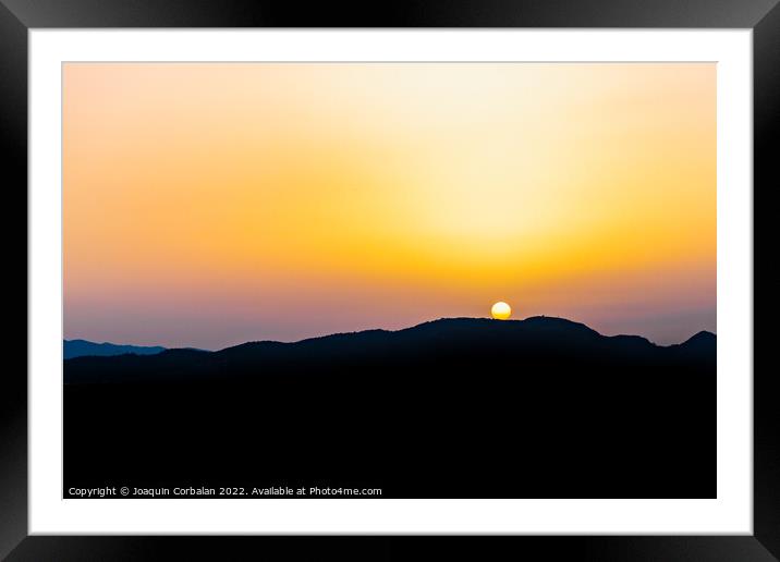 The hot sun hides behind the mountains on a summer day at dusk. Framed Mounted Print by Joaquin Corbalan