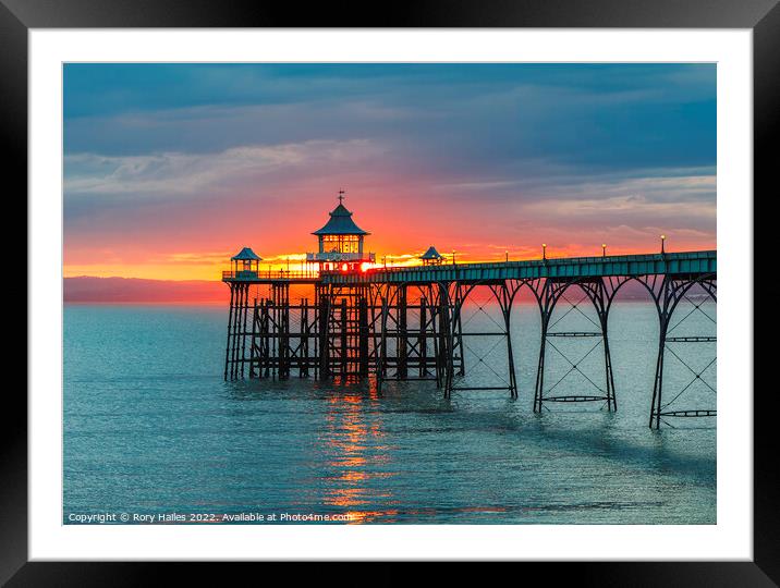 Clevedon Pier at sunset with a reddish orangey glow in the background Framed Mounted Print by Rory Hailes