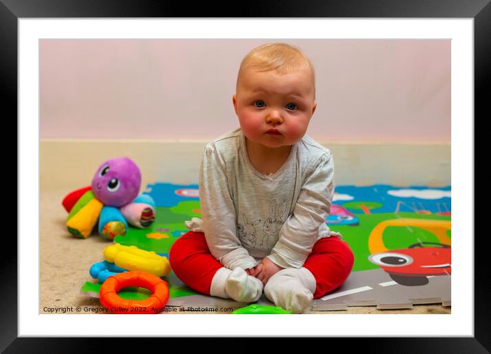 A baby girl sitting on a colourful mat with her toys Framed Mounted Print by Gregory Culley