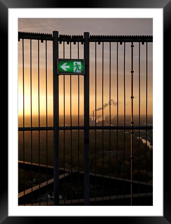 An emergency exit sign with an industrial site in the background Framed Mounted Print by Lensw0rld 