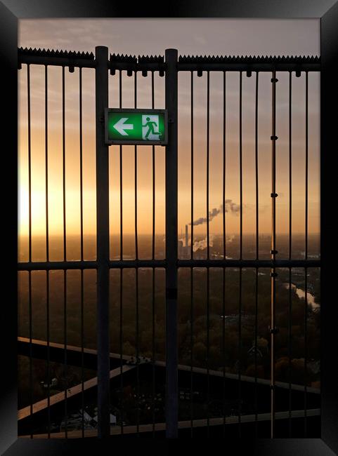 An emergency exit sign with an industrial site in the background Framed Print by Lensw0rld 