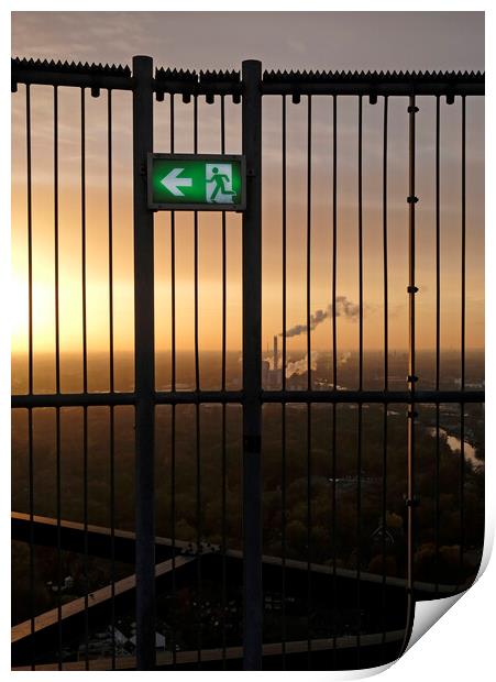 An emergency exit sign with an industrial site in the background Print by Lensw0rld 