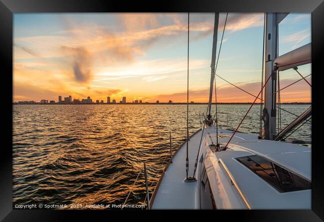 Yacht sailing towards cityscape on horizon at sunset Framed Print by Spotmatik 