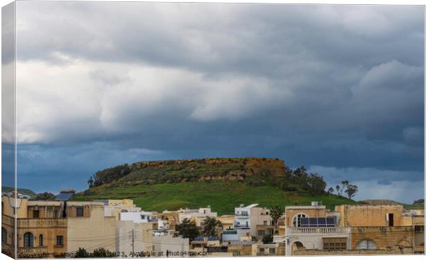 Storm over the hill with buildings, Gozo Island. Canvas Print by Maggie Bajada