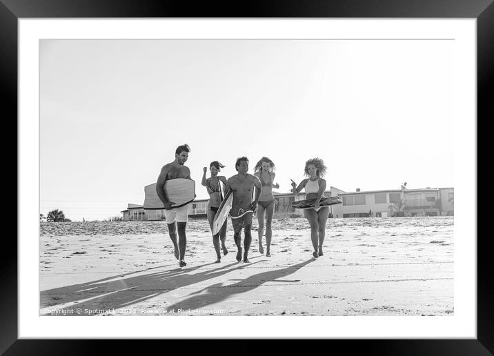 Friends in swimwear running carrying bodyboards on beach Framed Mounted Print by Spotmatik 