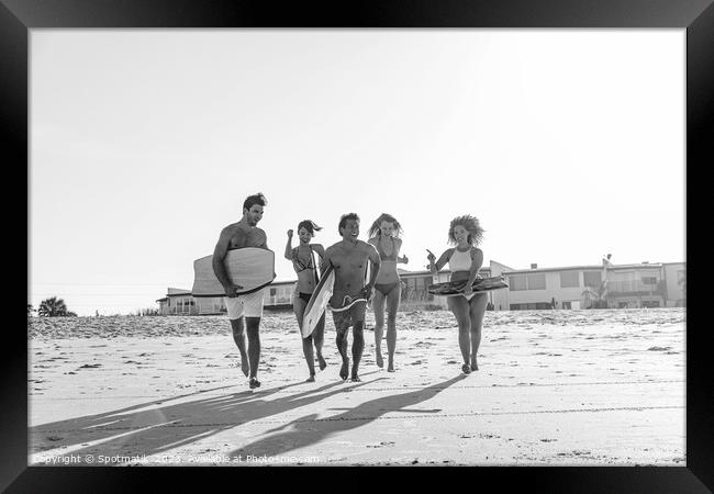 Friends in swimwear running carrying bodyboards on beach Framed Print by Spotmatik 