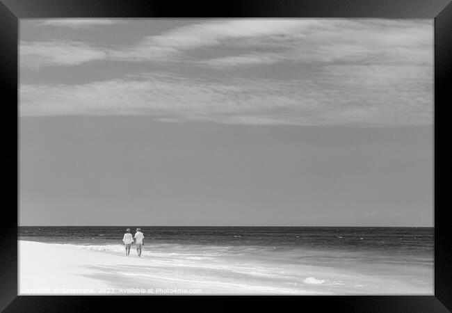 Mature couple walking along shoreline at beach resort Framed Print by Spotmatik 
