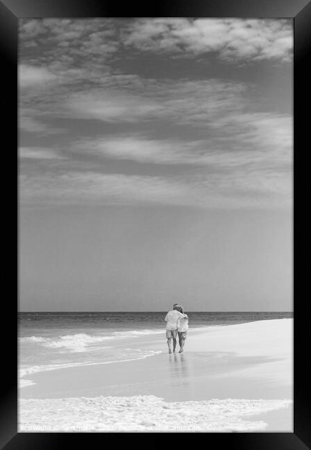 Retired couple walking by ocean in loving embrace Framed Print by Spotmatik 
