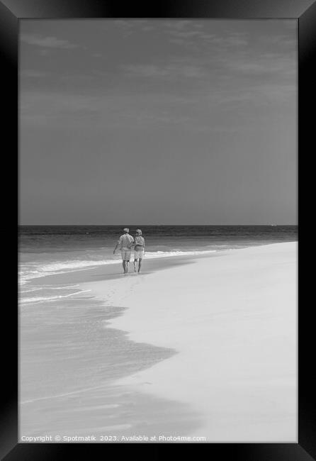 Tropical island shoreline with retired couple walking barefoot Framed Print by Spotmatik 