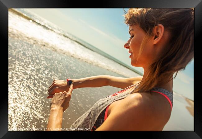 Caucasian female on ocean edge checking sports watch Framed Print by Spotmatik 