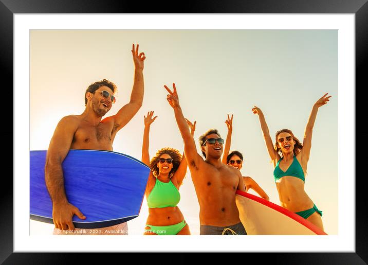Friends enjoying carefree fun going bodyboarding on beach Framed Mounted Print by Spotmatik 
