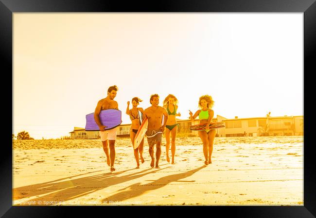 Friends in swimwear running carrying bodyboards on beach Framed Print by Spotmatik 