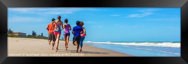 Panoramic view of friends jogging together on beach Framed Print by Spotmatik 