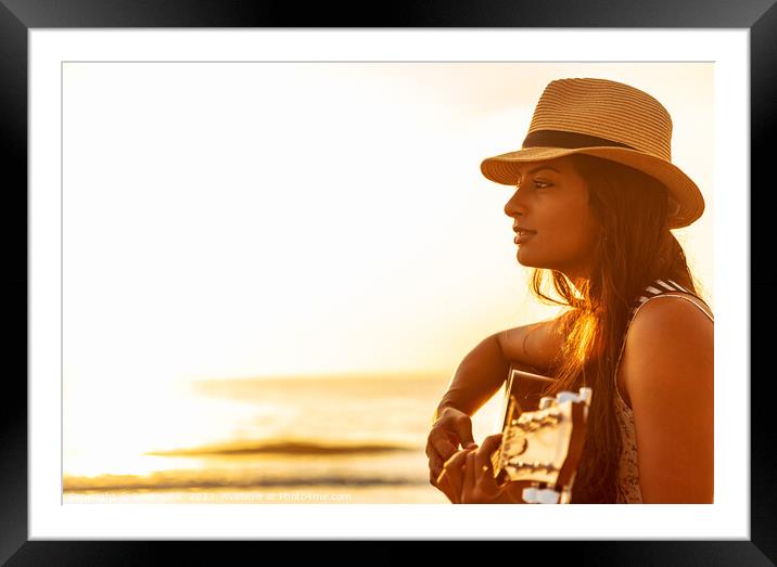 Indian woman wearing hat playing guitar on beach Framed Mounted Print by Spotmatik 