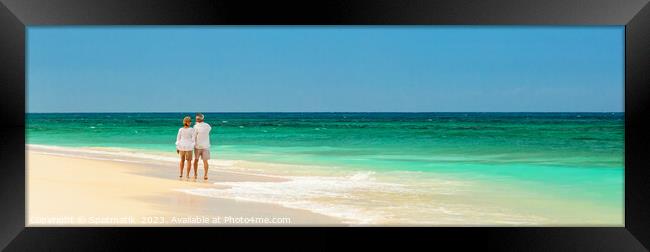 Panoramic view of mature couple walking on beach Framed Print by Spotmatik 