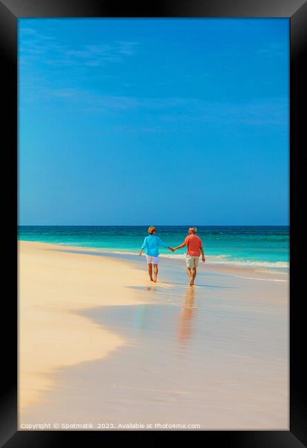 Retired couple holding hands enjoying walk on beach Framed Print by Spotmatik 