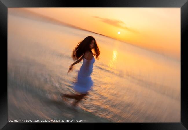 Motion blurred Asian girl dancing in ocean sunset Framed Print by Spotmatik 