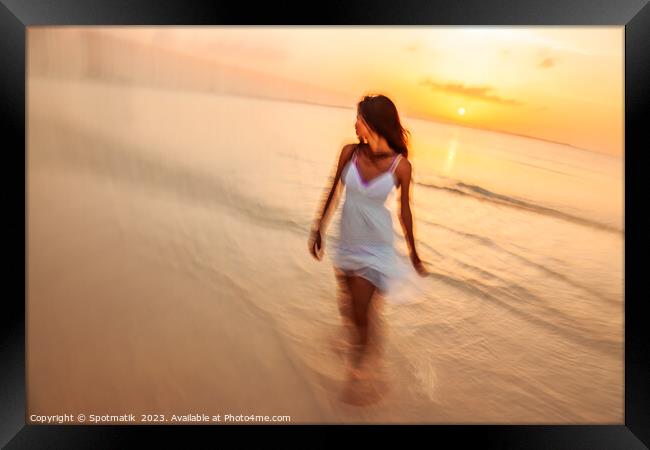 Motion blurred woman walking through waves at sunset Framed Print by Spotmatik 
