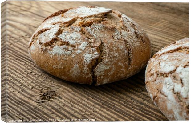Delicious baked bread on a wooden background Canvas Print by Lubos Chlubny