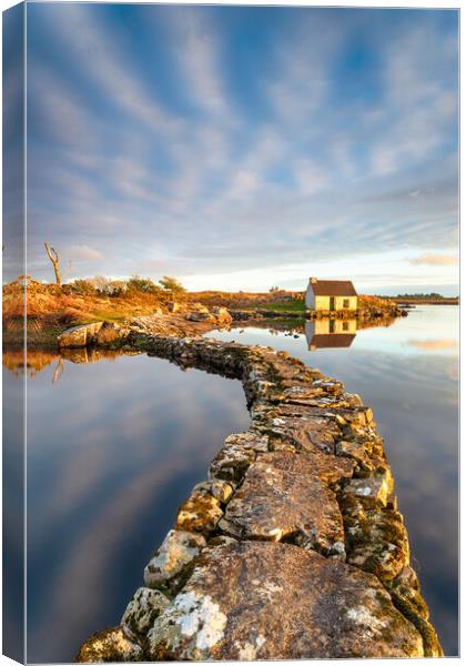 An old stone jetty across a lake leading to a small cottage Canvas Print by Helen Hotson