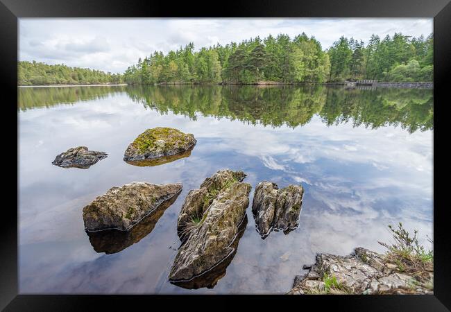 Jagged rocks pierce the still water on High Dam Ta Framed Print by Jason Wells