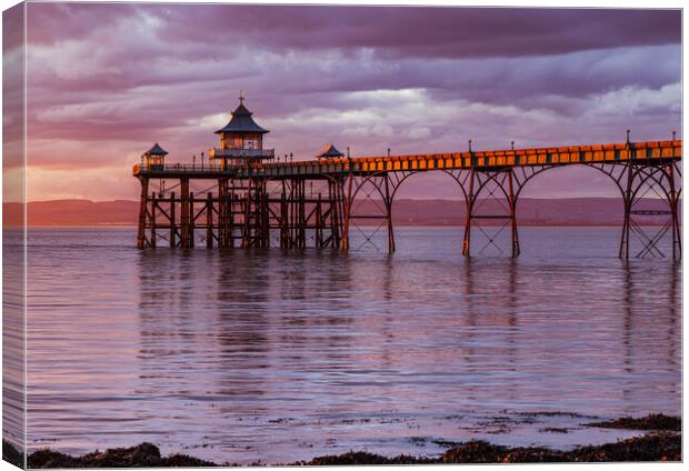 Clevedon Pier at sunset with a Pinkish hue in the sky and reflecting onto the sea Canvas Print by Rory Hailes