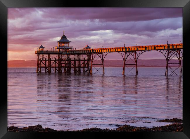 Clevedon Pier at sunset with a Pinkish hue in the sky and reflecting onto the sea Framed Print by Rory Hailes