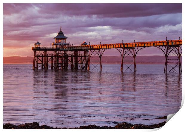 Clevedon Pier at sunset with a Pinkish hue in the sky and reflecting onto the sea Print by Rory Hailes