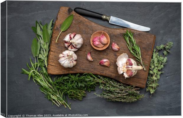 Still life, Garlic on a chopping board with herbs Canvas Print by Thomas Klee