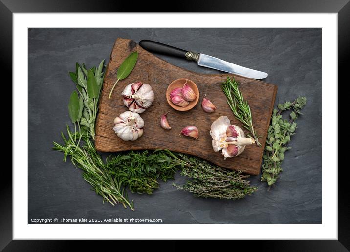 Still life, Garlic on a chopping board with herbs Framed Mounted Print by Thomas Klee