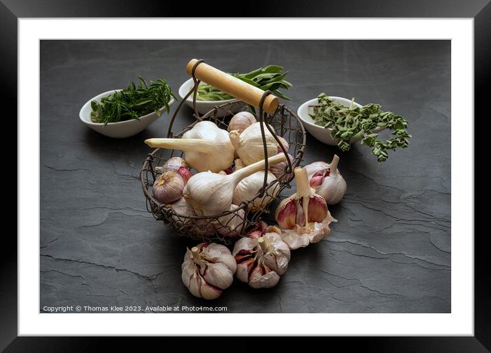 Still life, Garlic in a basket and fresh herbs on a slate plate Framed Mounted Print by Thomas Klee