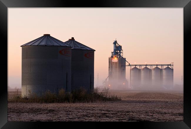 grain storage bins in a harvested soybean field with inland grain terminal in the background Framed Print by Dave Reede
