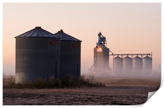 grain storage bins in a harvested soybean field with inland grain terminal in the background Print by Dave Reede